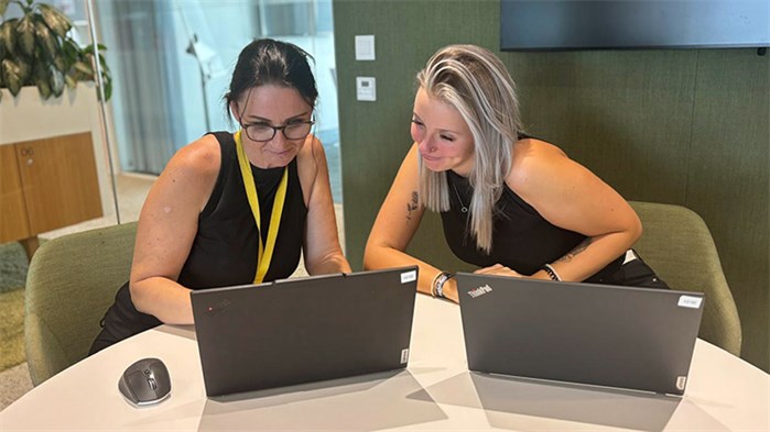 Zwei Postmitarbeiter*innen blicken auf Laptops